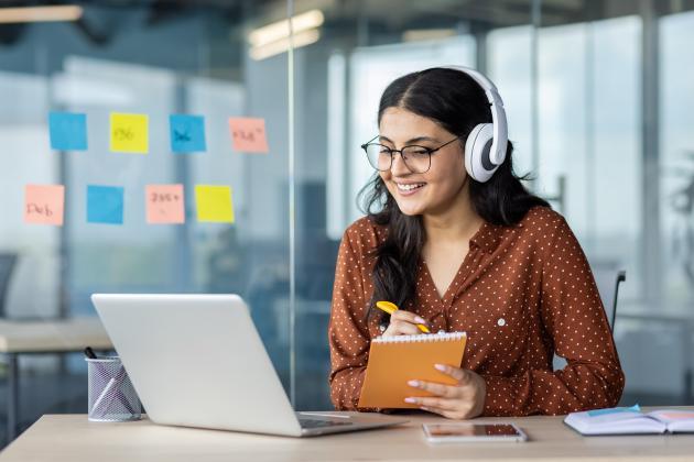 Woman wearing headphones with laptop and notebook